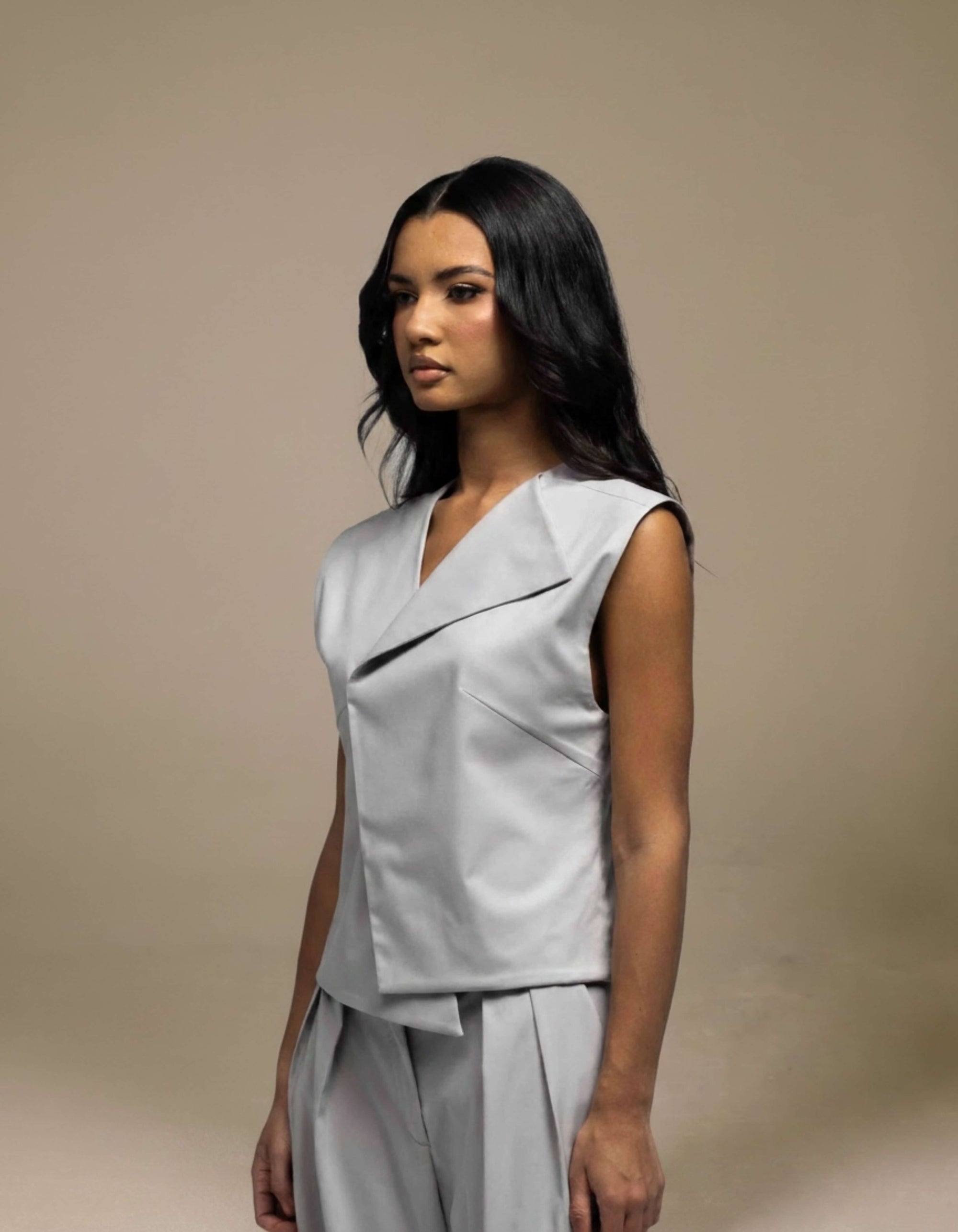 Sleeveless tailored grey top with structured fold neckline detail
