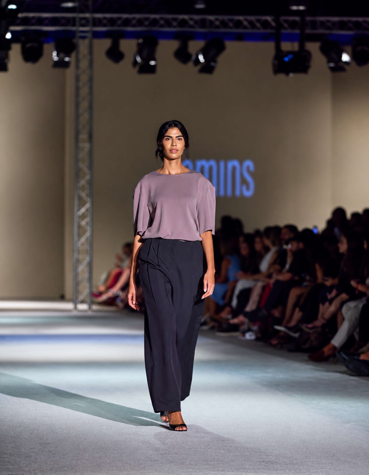 Front Runway View Of The Elamins Oversize T-Shirt In Taupe, Featuring Dropped Shoulders And A Relaxed Silhouette, Paired With The Elamins Black Pleated Trousers At TheEventDXB.