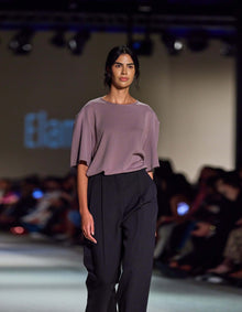 Side-Angle Runway View Of The Elamins Oversize T-Shirt In Taupe, Highlighting Its Fluid Drape And Oversized Shape, Paired With The Elamins Black Pleated Trousers At TheEventDXB.