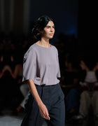 Side-Angle closeup Runway View Of The Elamins Oversize T-Shirt In Taupe, Highlighting Its Fluid Drape And Oversized Shape, Paired With The Elamins Black Pleated Trousers At TheEventDXB.