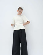 Model Wearing The Elamins Pleated Trousers In Black Styled With The Elamins Structured Hourglass Top In Off White, Highlighting The Contrast Between Wide-Leg Tailoring And A Sculpted Top.
