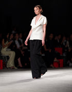 Model Wearing The Elamins Pleated Trousers In Black Paired With The Elamins Exaggerated Lapel Top In Off White On The Runway At TheEventDXB Fashion Show.