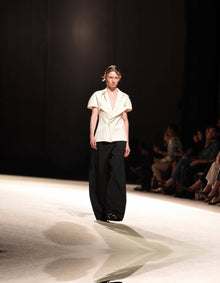 Full-Length Runway View Of The Elamins Pleated Trousers In Black, Featuring A Wide-Leg Silhouette, Styled With The Elamins Exaggerated Lapel Top In Off White At TheEventDXB.