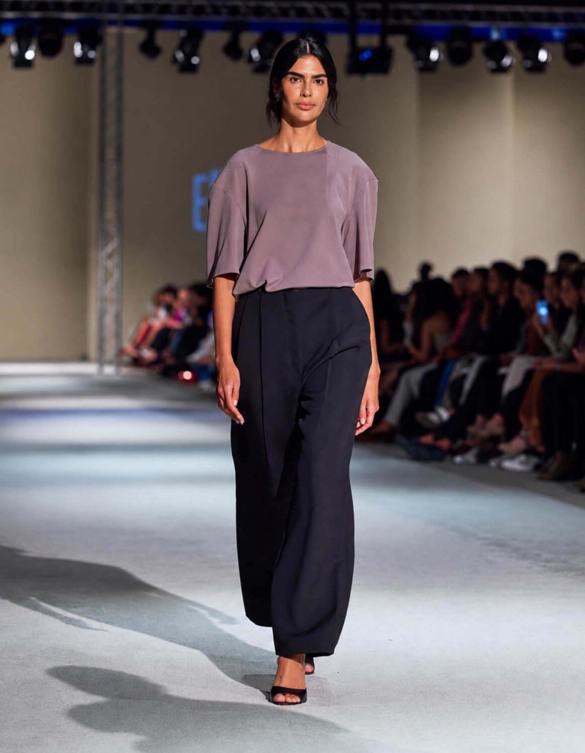 Model Wearing The Elamins Pleated Trousers In Black Styled With The Elamins Oversize T-Shirt In Taupe At TheEventDXB Fashion Show.