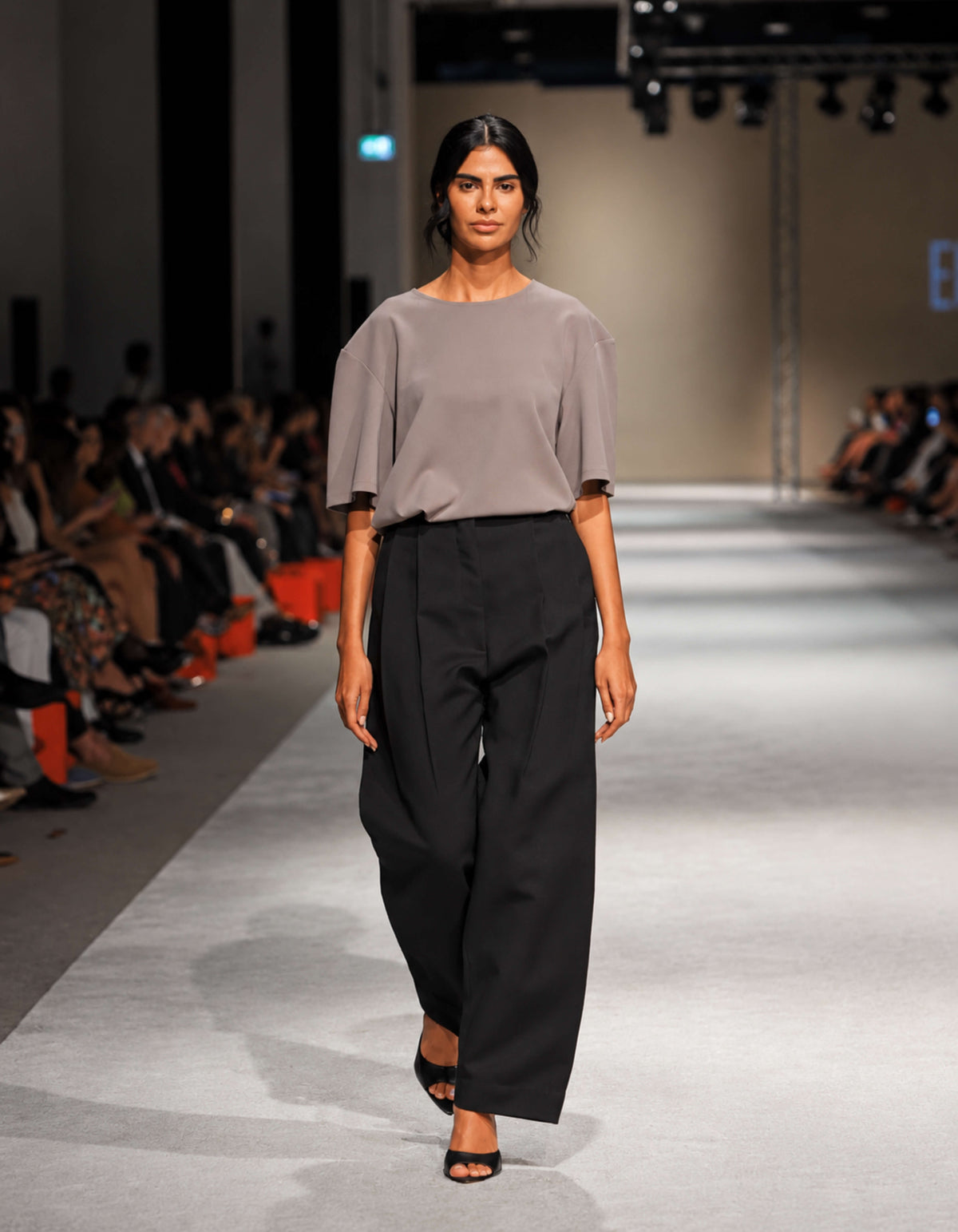 Full-Length Runway Photograph Of The Elamins Pleated Trousers In Black, Showing The Wide-Leg Shape And Fluid Movement With The Elamins Oversize T-Shirt In Taupe At TheEventDXB.