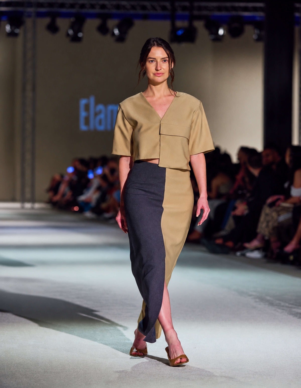 Model Walking At TheEventDXB Wearing The Elamins Vertical Two Tone Skirt In Tan And Denim With The Oversize Pocket Crop Top, Highlighting The Front Slit.